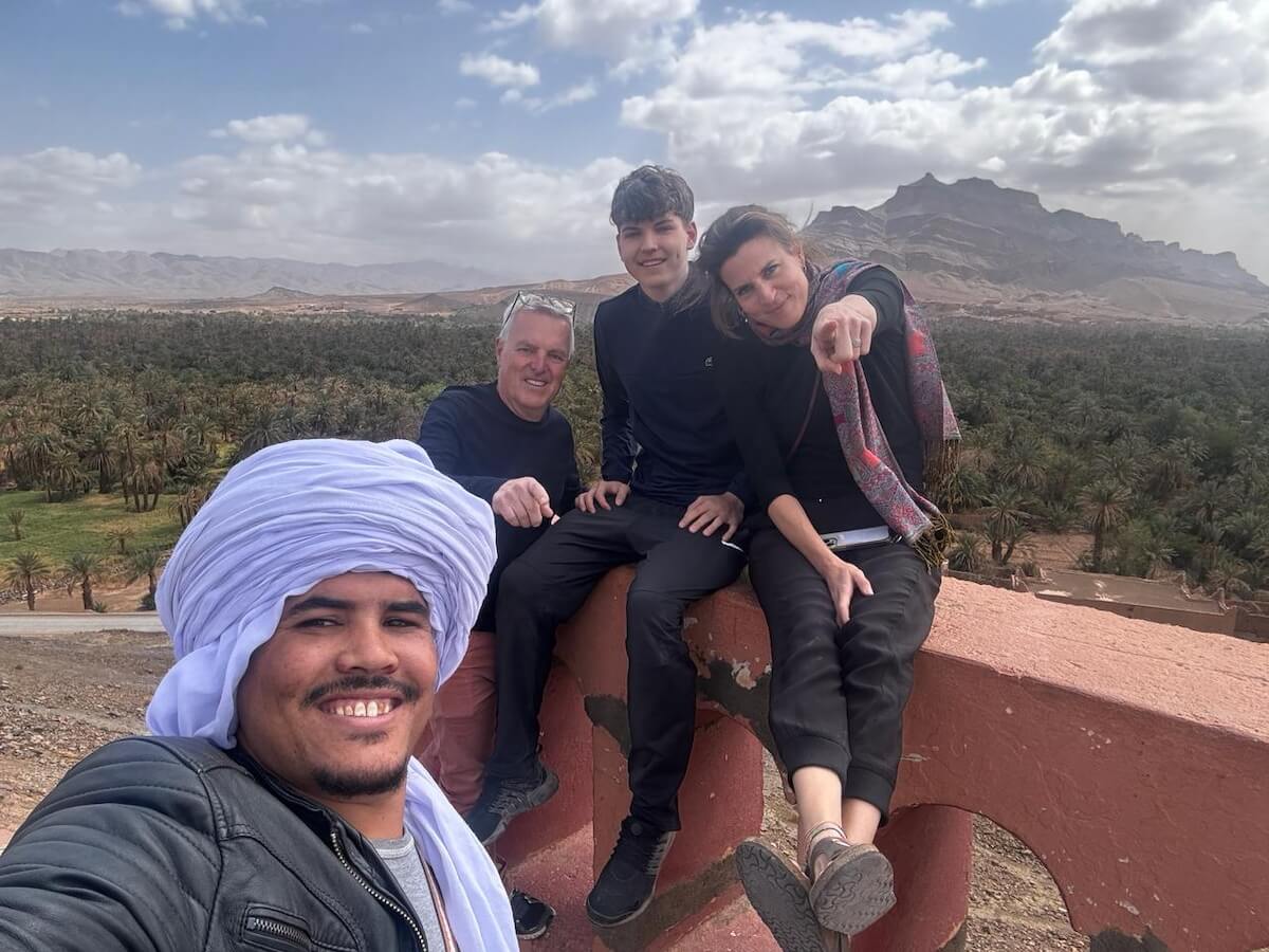 Ismail, Discover Sahara Tours guide, with smiling guests overlooking date palm oasis on custom excursion through morocco