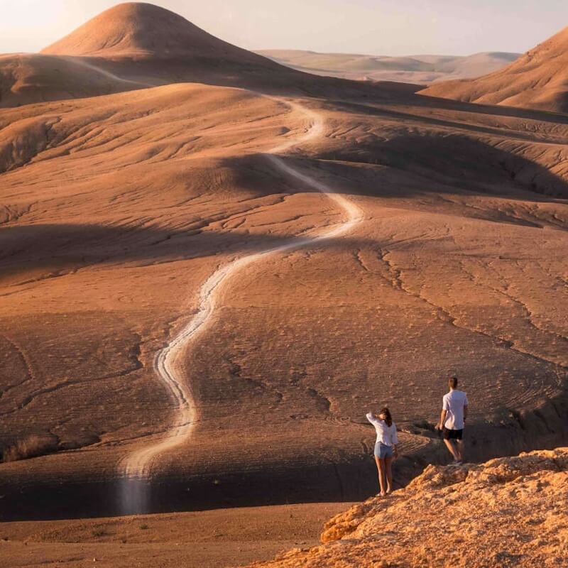 People on a cliff overlooking a road through the rocky dunes of the Agafay Desert in Morocco